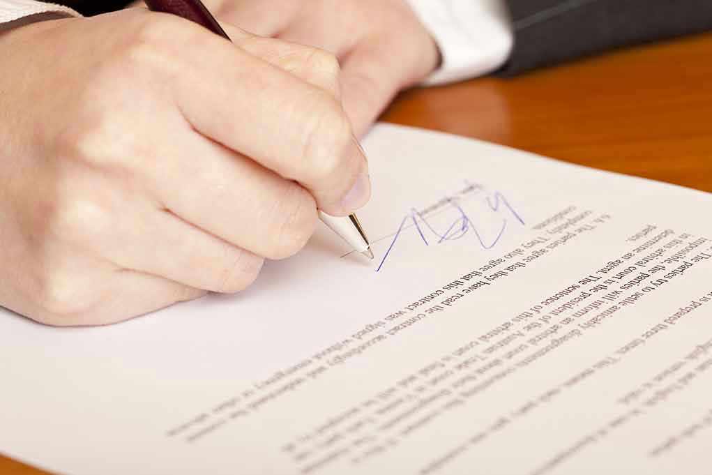 Hand signing a document with a pen.