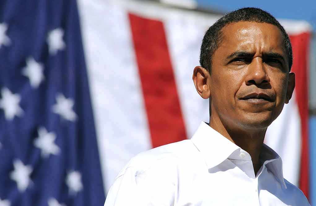 A man in a white shirt standing in front of an American flag