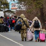 Mystery Flights Dump Refugees – Officials Baffled Group of people carrying luggage walking along a road with a soldier