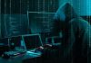 Hacker in dark room surrounded by computer screens.