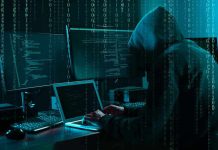 Hacker in dark room surrounded by computer screens.