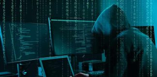 Hacker in dark room surrounded by computer screens.