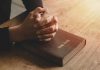 Hands praying on a Bible.