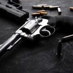 NFL Star FLEES Country After Shooting Revolvers and bullets on a dark surface.