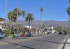 Street with cars, palm trees, and mountains in the background.