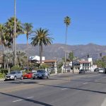 Street with cars, palm trees, and mountains in the background.