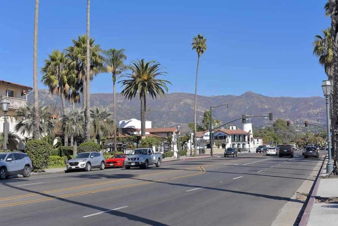 Street with cars, palm trees, and mountains in the background.