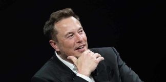 Man in suit smiling, resting chin on hand.