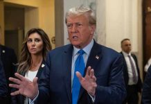 Trump Suffers Setback – Judge DENYS His Pick Man speaking with hands raised, woman and security behind.