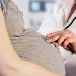 Doctor uses stethoscope on pregnant womans belly.