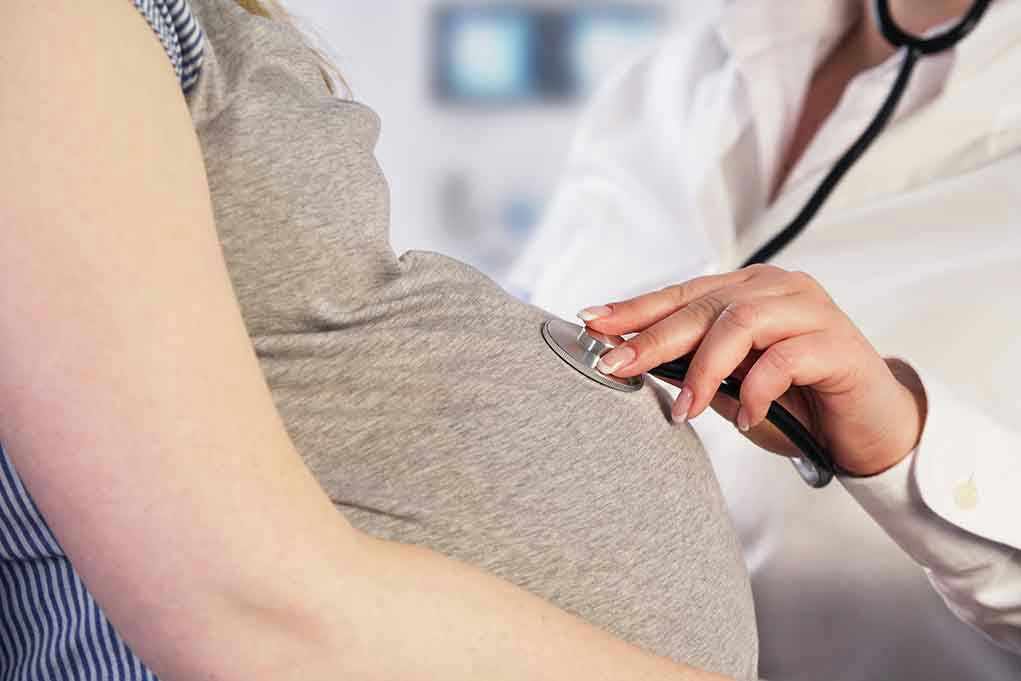 Doctor uses stethoscope on pregnant womans belly.