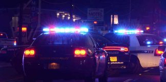 Police cars with flashing lights at a nighttime scene near a motel