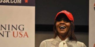 A woman wearing a red cap and a white blouse speaking at a political event