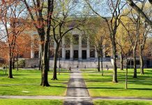 Students walking on a university campus with autumn trees and a historic building in the background