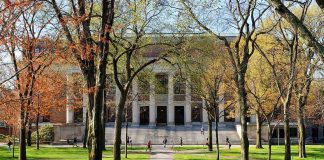 Students walking on a university campus with autumn trees and a historic building in the background