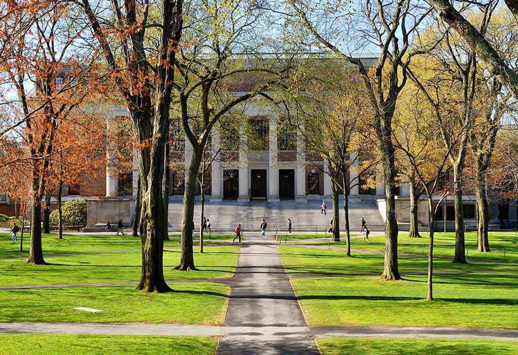 Students walking on a university campus with autumn trees and a historic building in the background