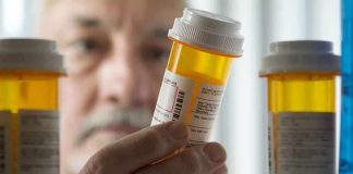 An elderly man holding a prescription bottle while examining it closely