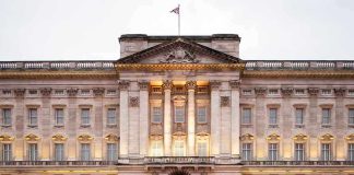 Front view of Buckingham Palace with illuminated facade and British flag