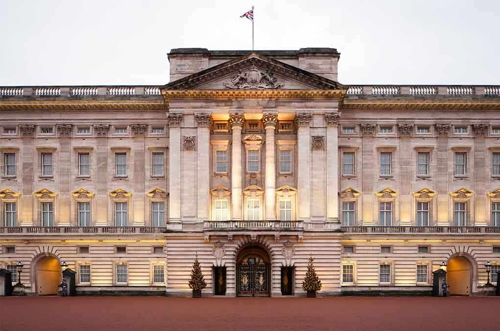 Front view of Buckingham Palace with illuminated facade and British flag