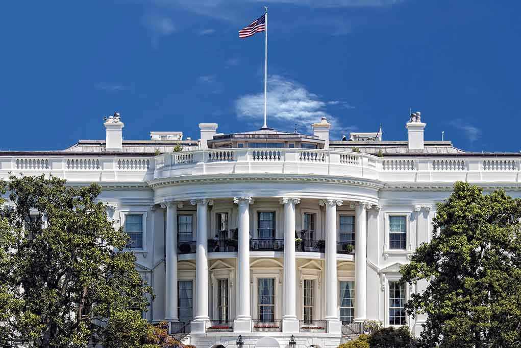 The White House with the American flag flying against a blue sky
