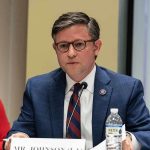 A public official speaking at a meeting with a nameplate in front of him