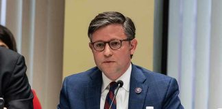 A public official speaking at a meeting with a nameplate in front of him