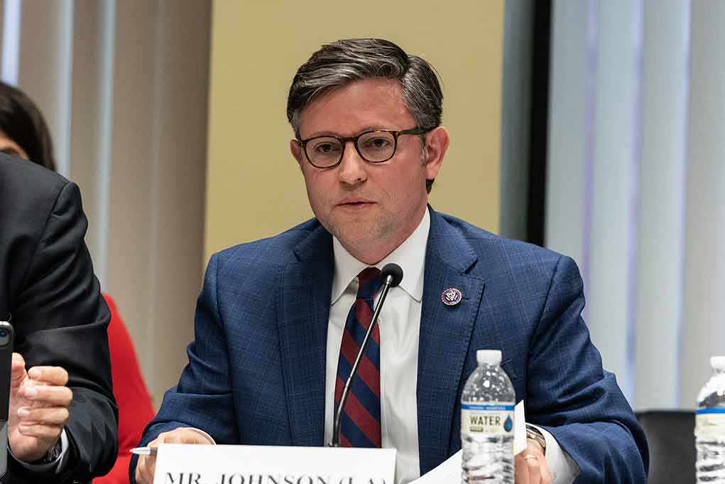 A public official speaking at a meeting with a nameplate in front of him