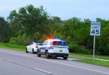 Police car with flashing lights pulling over a white vehicle beside a speed limit sign