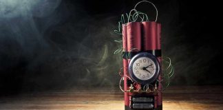 A stick of dynamite with a clock timer and wires, set against a dark smoky background