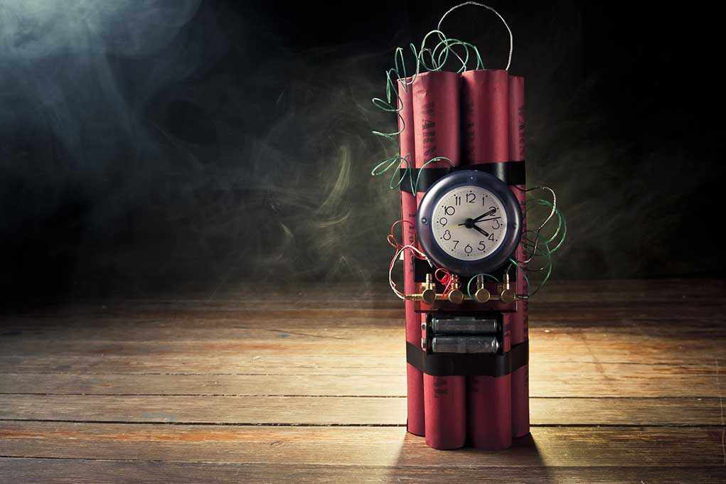 A stick of dynamite with a clock timer and wires, set against a dark smoky background