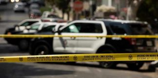 Police tape blocking street with patrol cars.