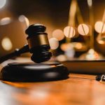 Gavel on wooden table with scales in background.