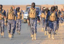 Camouflaged soldiers wearing masks and vests walk in desert.