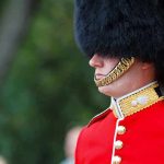 British soldier in ceremonial uniform with a black fur hat standing guard