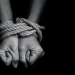 Two hands tightly bound with rope against a dark background