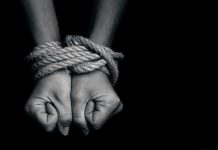 Two hands tightly bound with rope against a dark background