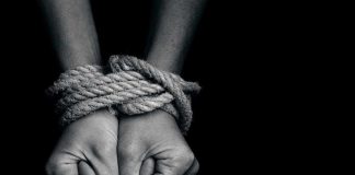 Two hands tightly bound with rope against a dark background