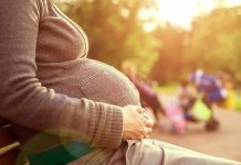 Pregnant woman sitting on a bench in a park during sunset