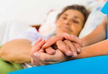 A caregiver holding the hands of an elderly patient in a hospital bed