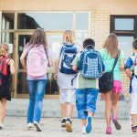 Group of children walking towards a school entrance with backpacks