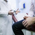 A doctor in a white coat discussing with a patient sitting on an examination table