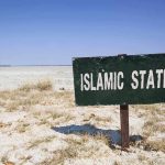 A weathered sign reading 'ISLAMIC STATE' in a barren landscape
