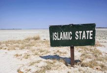 A weathered sign reading 'ISLAMIC STATE' in a barren landscape