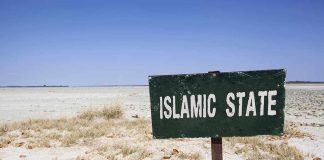 A weathered sign reading 'ISLAMIC STATE' in a barren landscape