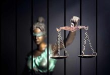 Blindfolded Lady Justice statue holding scales behind bars.