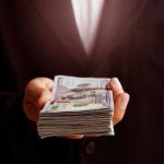 Inheritance Letters Target Seniors—Then The Trap Hand holding a stack of hundred-dollar bills.