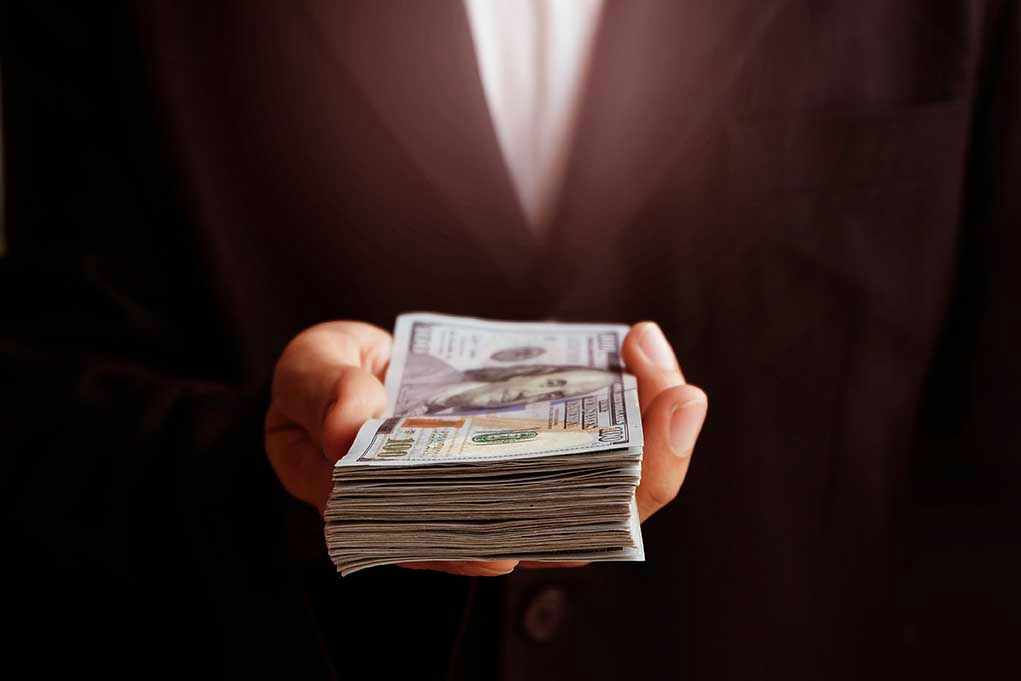 Hand holding a stack of hundred-dollar bills.