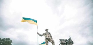 Soldier on tank holding Ukrainian flag.