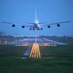 An airplane approaching the runway at night with landing lights illuminated