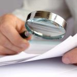 A hand holding a magnifying glass over a document